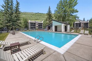 A swimming pool with lounge chairs, a deck, and a building with balconies. - C14 Gore Creek Meadows 3 Bedroom Condo by RedAwning (Vail)