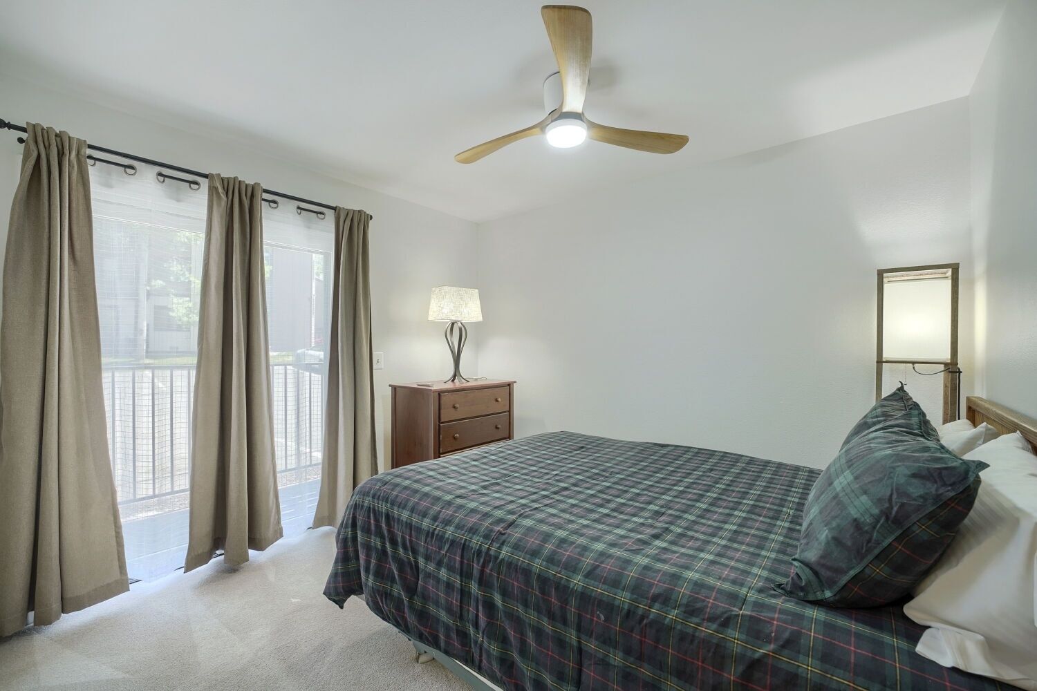A bedroom with a bed, a nightstand, a lamp, a ceiling fan, and a window with curtains.