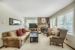 A living room with a sofa, armchair, coffee table, fireplace, television, and large windows. - C14 Gore Creek Meadows 3 Bedroom Condo by RedAwning (Vail)