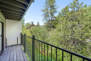 A wooden deck with a black railing, overlooking a dense forest with various trees and shrubs. - C14 Gore Creek Meadows 3 Bedroom Condo by RedAwning (Vail)