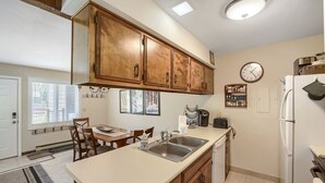 A kitchen with wooden cabinets, a white countertop, a sink, a refrigerator, and a dining area with a table and chairs.