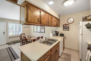 A kitchen with wooden cabinets, a white countertop, a sink, a refrigerator, and a dining area with a table and chairs. - C14 Gore Creek Meadows 3 Bedroom Condo by RedAwning (Vail)