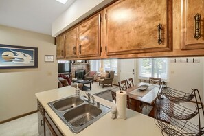 A kitchen with wooden cabinets, a double sink, and a dining area with a table and chairs. - C14 Gore Creek Meadows 3 Bedroom Condo by RedAwning (Vail)