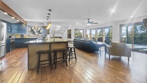 Een moderne keuken met een centraal eiland, houten vloeren en grote ramen met uitzicht op de omgeving.