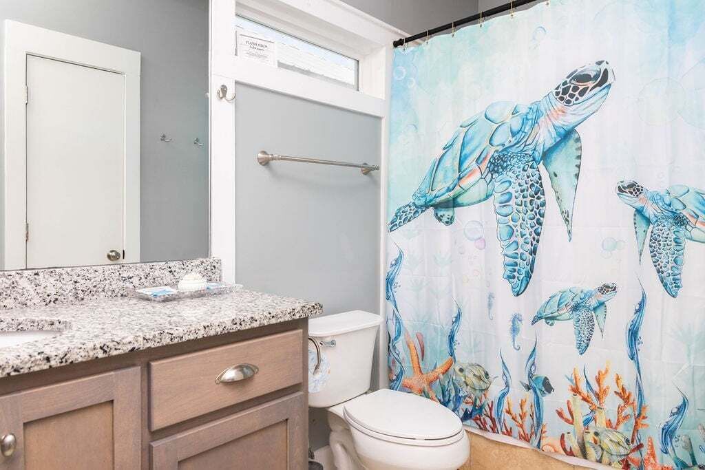 A bathroom with a shower curtain featuring sea turtles and coral, a granite countertop, and a white toilet.