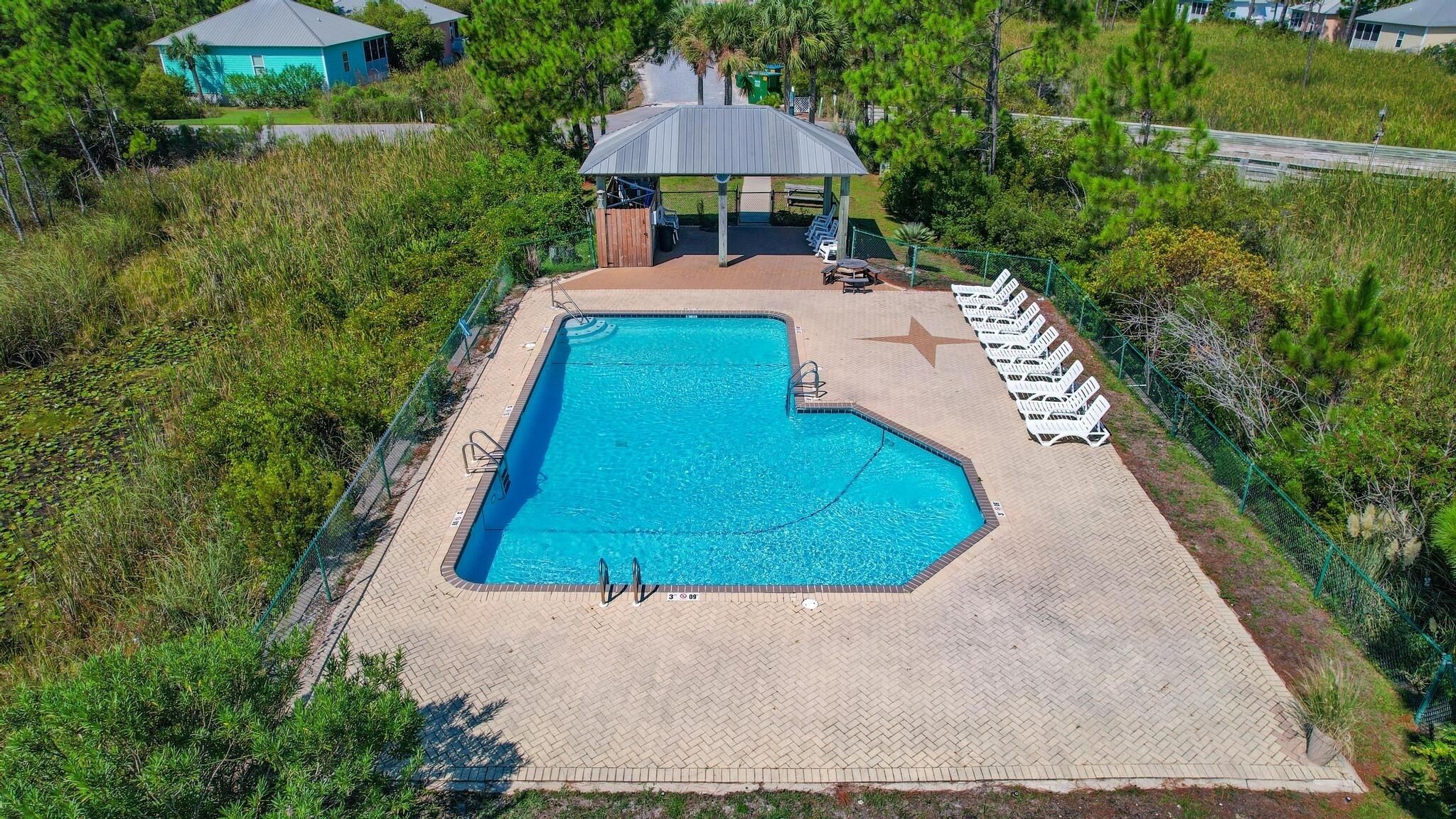 An outdoor swimming pool with a gazebo, lounge chairs, and a paved deck.