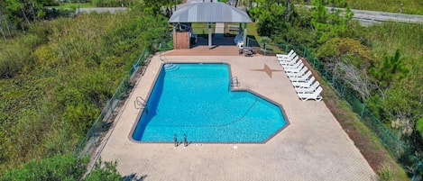 An outdoor swimming pool with a gazebo, lounge chairs, and a paved deck.