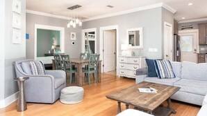 Un salón comedor amplio con un sofá gris, una mesa de centro de madera y una zona de comedor con mesa y sillas de madera.