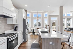 Une cuisine moderne avec des meubles blancs, un grand îlot central, un four encastré et un coin repas offrant une vue agréable.
