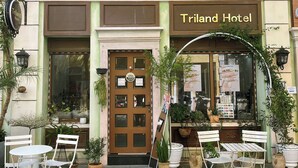 The exterior of Triland Hotel with a traditional facade, a central entrance door, and outdoor seating area with white chairs and tables. - Triland (Phu Quoc)