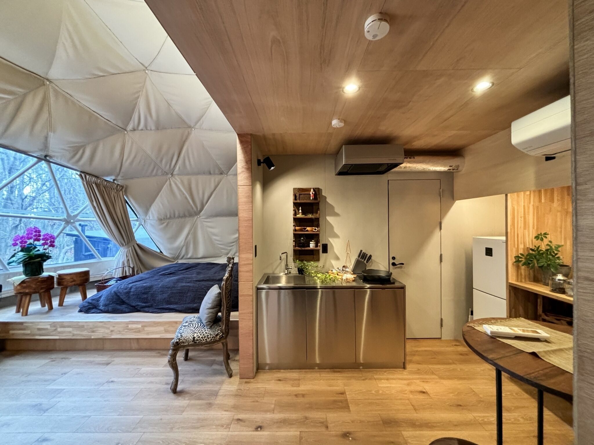 Um espaço de estar compacto e moderno, com cozinha, mesa de jantar e área de estar com vista através de uma grande janela.