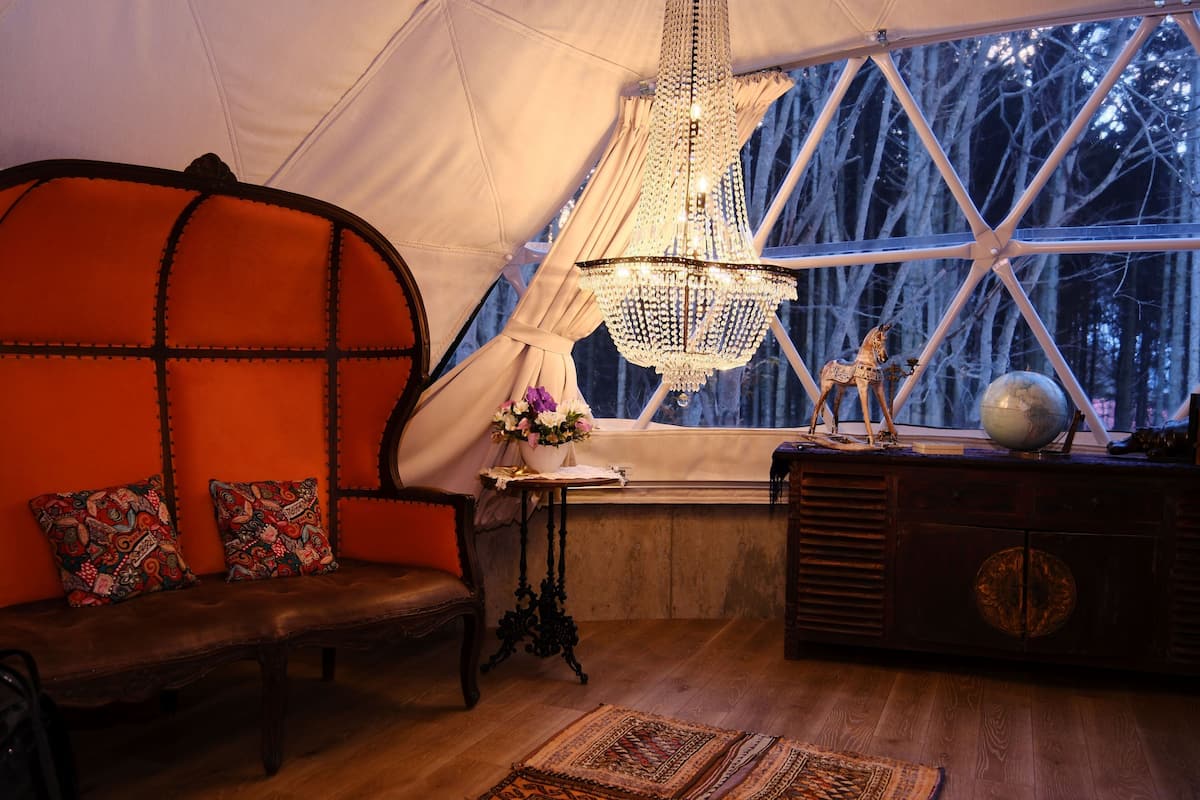 A cozy interior with a wooden bench, a chandelier, a globe, and a window with a view of trees.