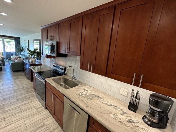A modern kitchen with dark wooden cabinets, a stainless steel sink, and a marble countertop.