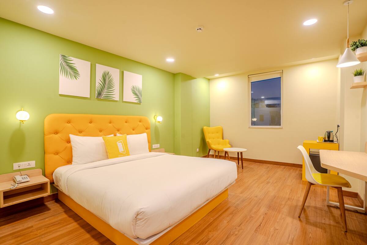 A hotel room with a large bed, a small table, a chair, and a window.