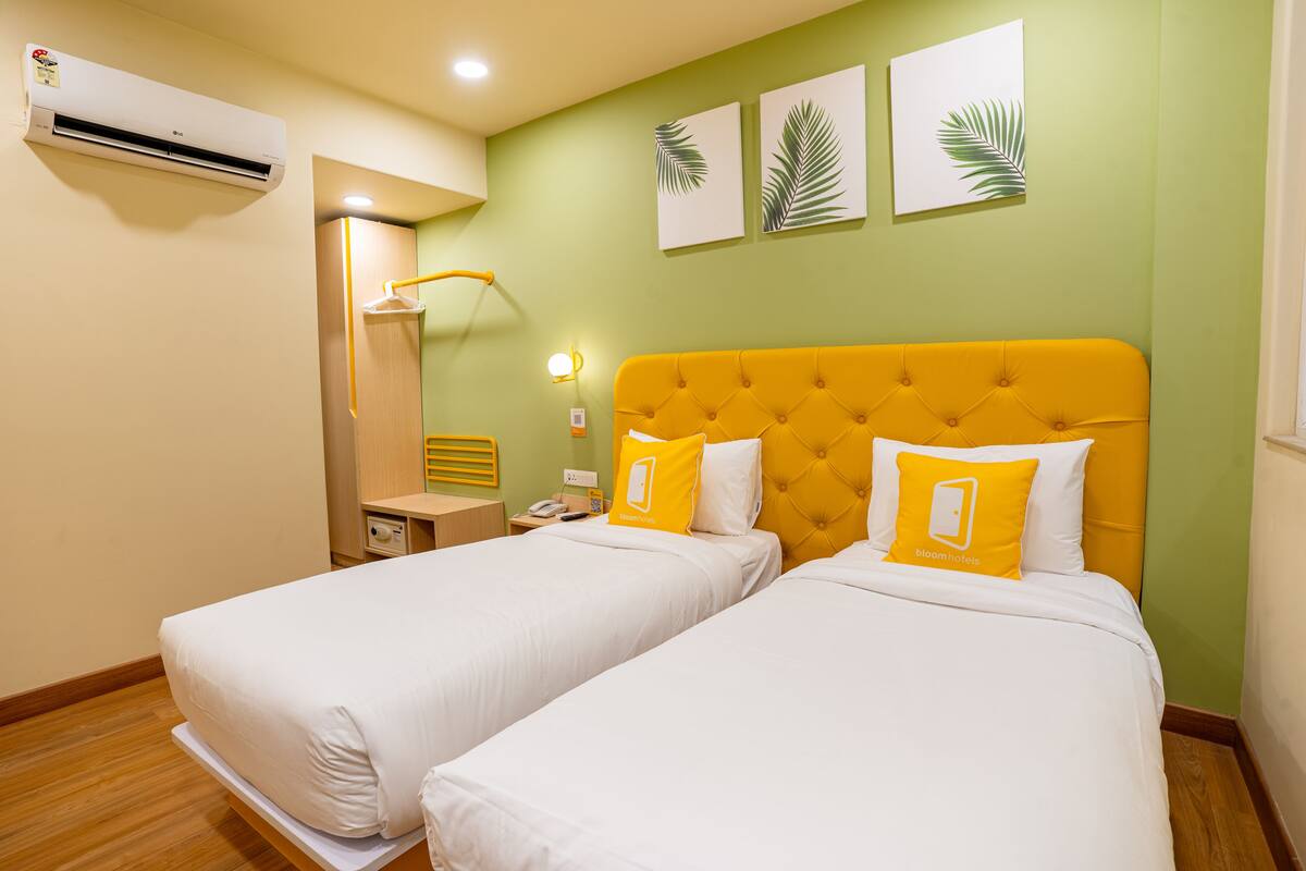 A hotel room with two beds, a bright yellow headboard, and a green wall with leaf decorations.