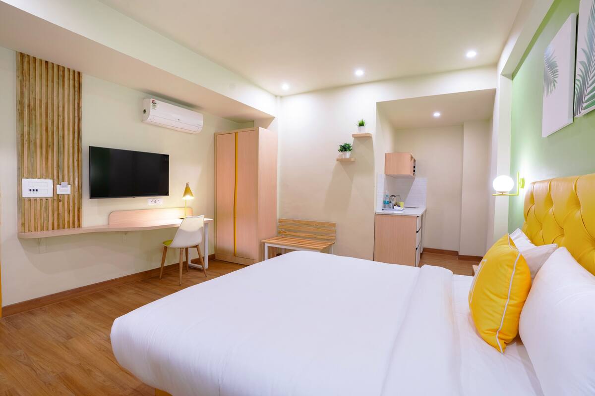 A hotel room with a bed, a desk, a TV, a wardrobe, and a small kitchenette.