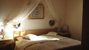 Un dormitorio con cama con dosel, una mesita de noche con lámpara, un cuadro enmarcado en la pared y una pequeña mesita de noche con reloj.
