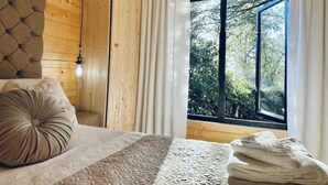 Ein Schlafzimmer mit einem Bett, einem Fenster mit Vorhängen und Blick auf Bäume.