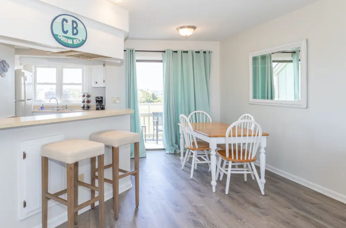 A kitchen with a CB sign, a dining area with a wooden table and white chairs, and a view through a glass door.