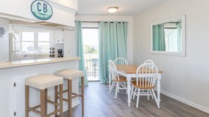 A kitchen with a CB sign, a dining area with a wooden table and white chairs, and a view through a glass door.