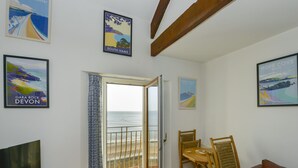 Una habitación con televisión, una mesa de madera, un sofá de cuero marrón y vista al mar a través de un ventanal.