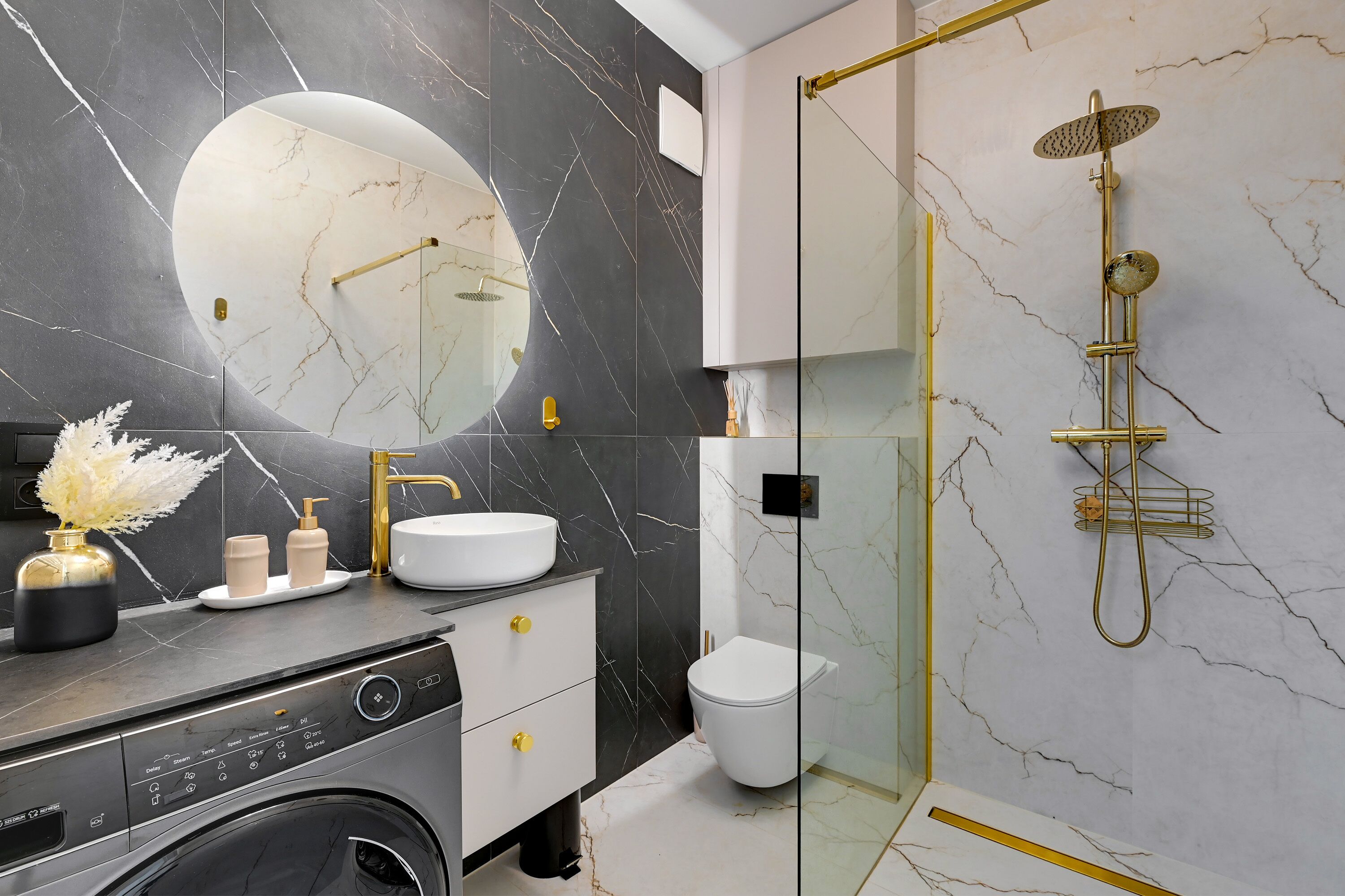 A modern bathroom with a marble backsplash, a round mirror, a gold showerhead, and a washing machine.