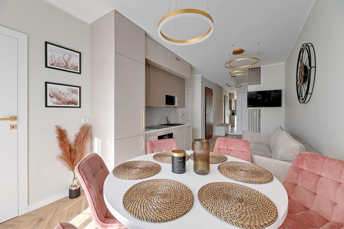 A modern dining area with a round table, pink upholstered chairs, and woven placemats.