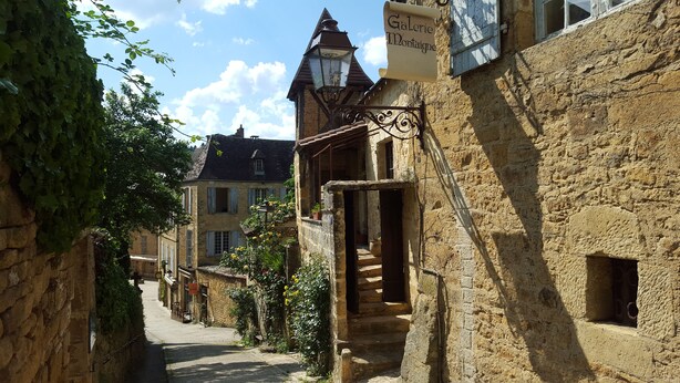 A narrow street with stone buildings, a visible entrance to a building with a sign, and a traditional lantern. - Au Coeur de Sarlat, L'appart d'à Coté...1 Chambre (Sarlat-la-Canéda)