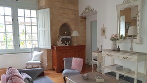 A living room with a sofa, armchair, and a coffee table. There is a fireplace with a mantel, a mirror, and a small table with a lamp. - Au Coeur de Sarlat, L'appart d'à Coté...1 Chambre (Sarlat-la-Canéda)