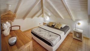 Un dormitorio con techo inclinado, una cama con ropa de cama estampada, lámparas de noche y una mesa de madera con un jarrón y un cuenco.