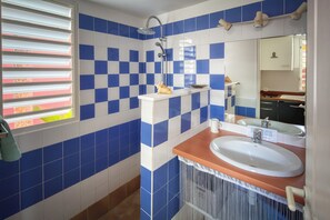 Ein Badezimmer mit blauen und weißen Karokacheln, einer Dusche, einem Waschbecken mit Spiegel und einem Fenster mit Jalousien.