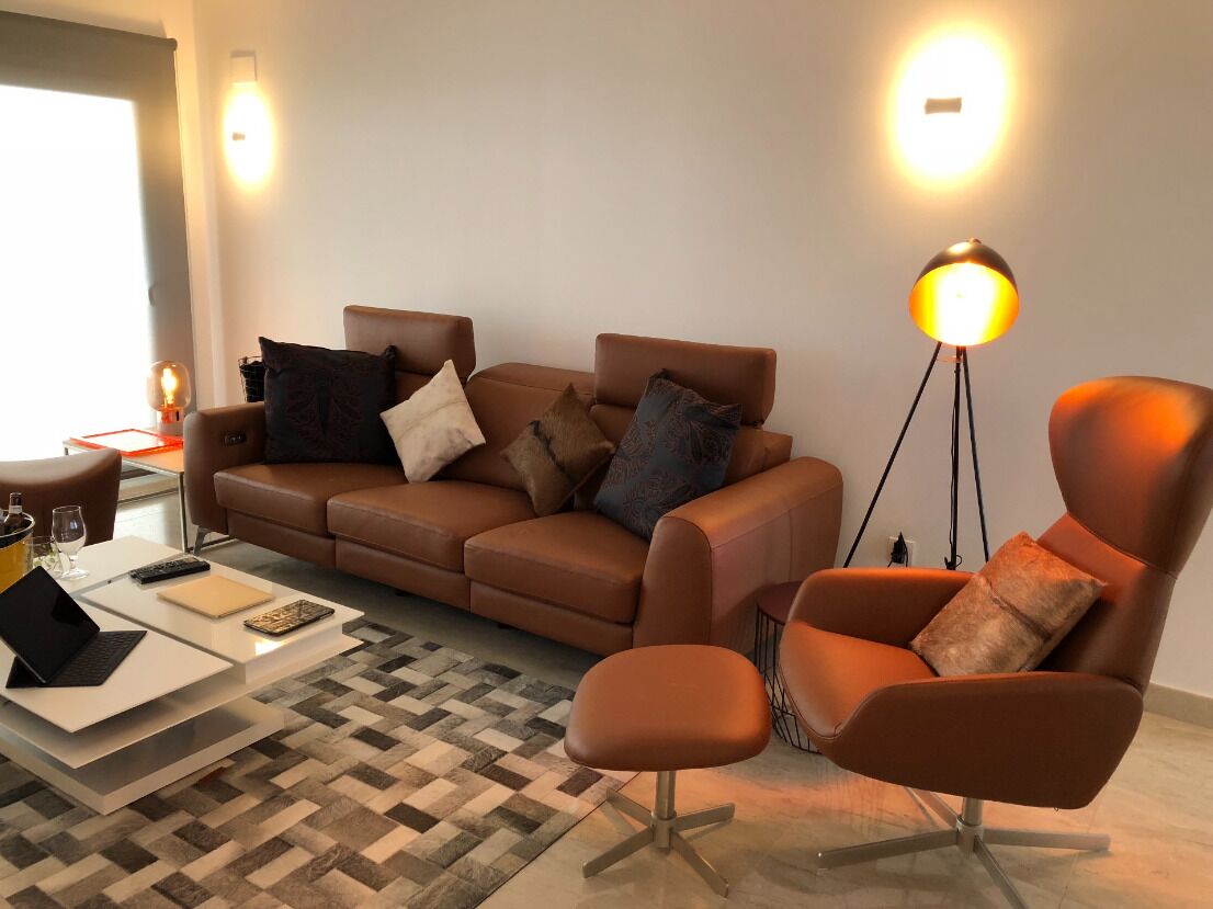 Una sala de estar moderna con un sofá de cuero marrón, un sillón a juego, una pequeña mesa de centro y una lámpara de pie.