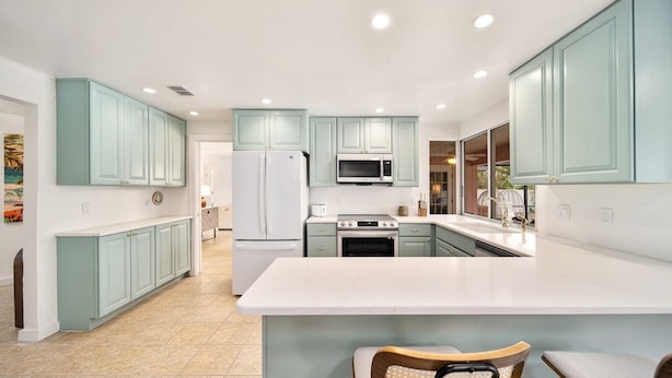 A modern kitchen with teal cabinets, white countertops, and a central island with seating. - Sooner Beach Escape: Cute Pool Home in East Rocks (Sanibel)