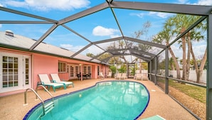 A covered swimming pool with lounge chairs and a patio area. - Sooner Beach Escape: Cute Pool Home in East Rocks (Sanibel)