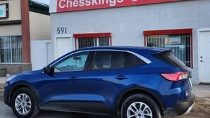 Een blauwe auto geparkeerd voor een gebouw met een bord waarop staat 'Chessings Car Rental'.