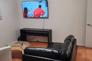 Un salon avec un canapé en cuir noir, une petite table ronde et un téléviseur fixé au mur.