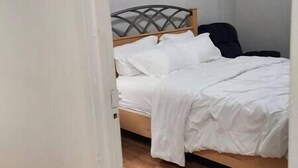 Een bed met een houten hoofdeinde en wit beddengoed in een kamer met effen muren.