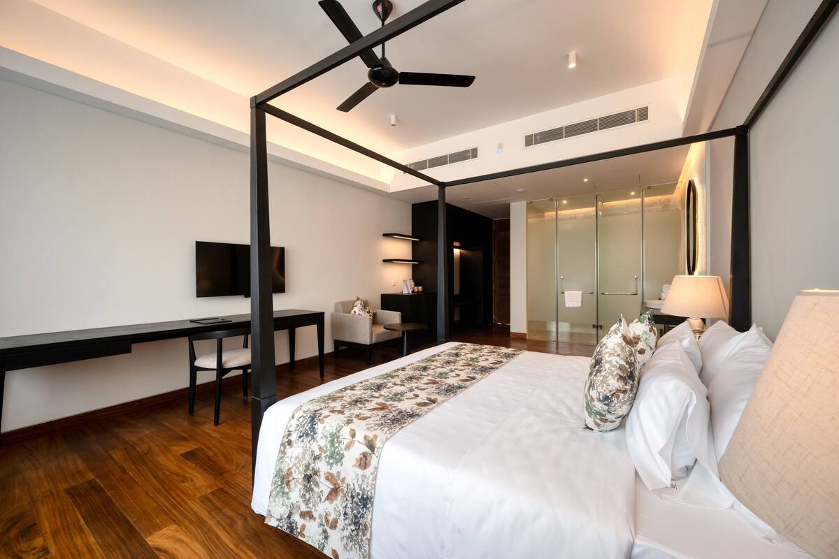 A modern hotel room with a bed, a desk, a chair, a television, and a ceiling fan.