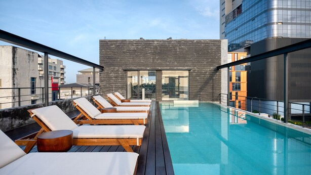 A rooftop pool area with sun loungers and a modern building in the background. - Taprobane House (Colombo)