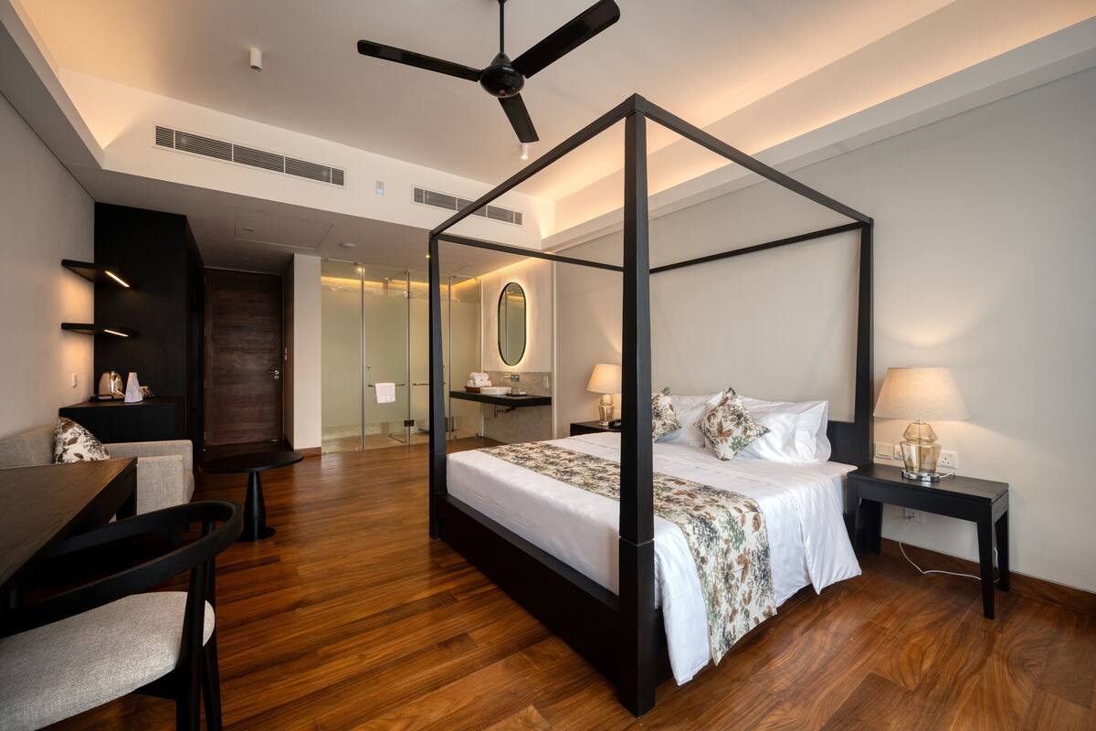A modern bedroom with a four-poster bed, a desk, and a chair.