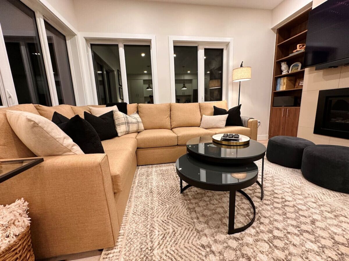 A living room with a beige sectional sofa, a black coffee table, and a fireplace.