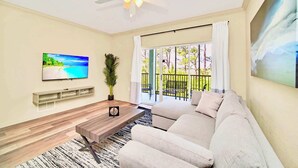 A living room with a sofa, TV, wooden coffee table, and a ceiling fan. - Upstay 3BR Suite w Pool, Sauna & Games—Near Disney (Winter Garden)