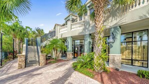A multi-story hotel with a brick pathway leading to the entrance, surrounded by palm trees and greenery. - Near Disney - Family Condo w Pool, Games, and More (Winter Garden)