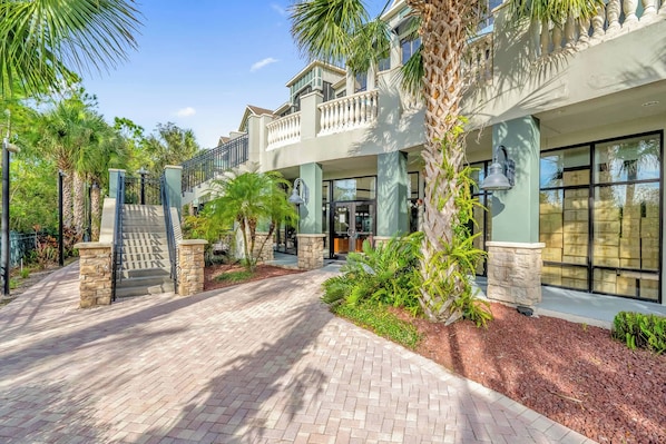 A multi-story hotel with a brick pathway, palm trees, and a gated entrance.
