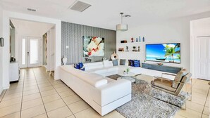A modern living room with a white sofa, a flat-screen TV, and a patterned wall. - Upstay Lakefront Home w Pool, Game Room and BBQ (Kissimmee)