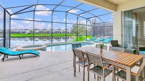 A pool area with lounge chairs, a table, and a hot tub, surrounded by a glass enclosure with a view of houses and a lake. - Upstay Lakefront Home w Pool, Game Room and BBQ (Kissimmee)