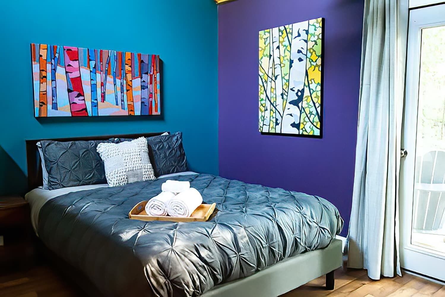 Un dormitorio con una cama, almohadas, una bandeja con toallas y dos obras de arte en las paredes.
