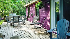 Une terrasse en bois avec des meubles d’extérieur, un barbecue et un bâtiment violet doté d’une porte-fenêtre coulissante.