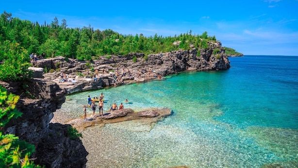 Une côte rocheuse bordée d’une eau turquoise cristalline, d’une végétation luxuriante, et où l’on peut voir des gens se détendre sur la plage.