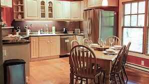 Une cuisine moderne avec des meubles en bois, une table à manger pour quatre personnes et une grande fenêtre laissant entrer la lumière naturelle.